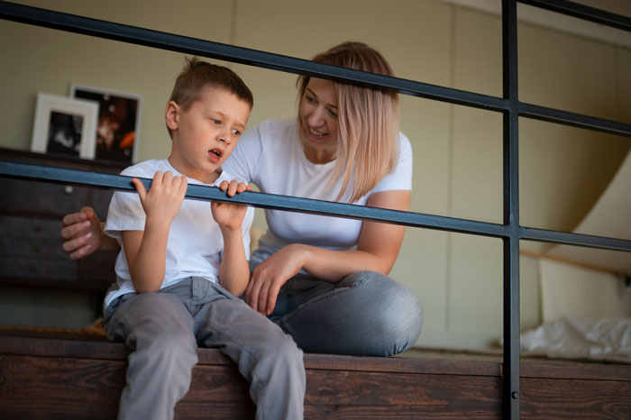 Young mom and her son sitting on stairs indoors, illustrating a scene related to unhinged mom at trampoline park.