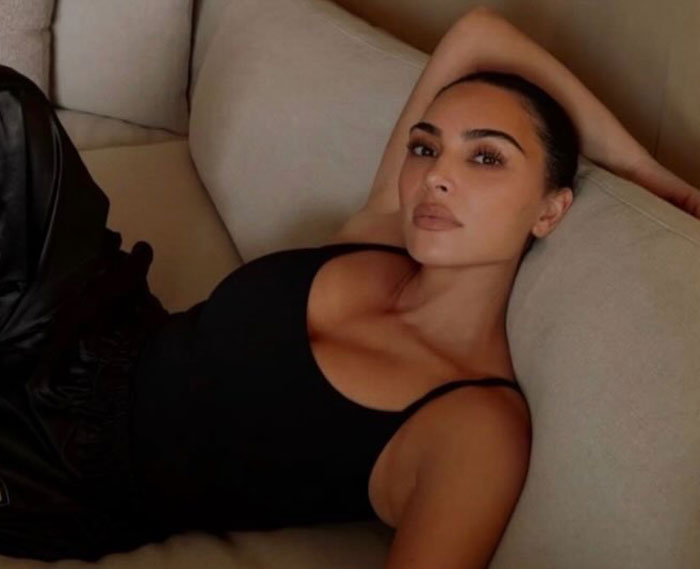 Kim Kardashian reclining on a beige couch wearing a black tank top, illustrating body language expert analysis of controlled moves.