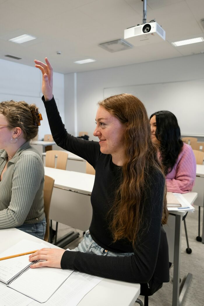 Young woman raising hand in classroom setting, illustrating people admit they silently judge others behavior concept.