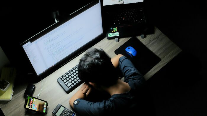 Person asleep at a desk with a laptop and smartphone, illustrating the most dangerous things often dismissed.