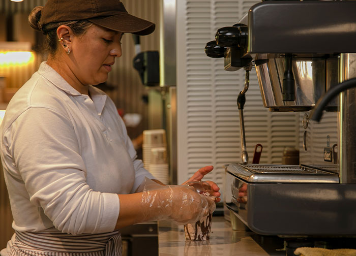 Woman in a coffee shop wearing gloves and a cap, preparing a drink next to an espresso machine, divorce lawyers concept.
