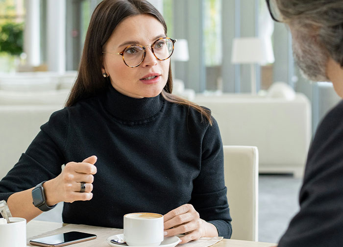 Divorce lawyer wearing glasses discussing serious cases with a client over coffee in a bright modern office.
