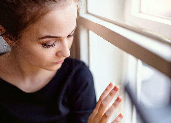 Young woman looking out window with a sad expression, evoking feelings described by divorce lawyers in haunting stories.
