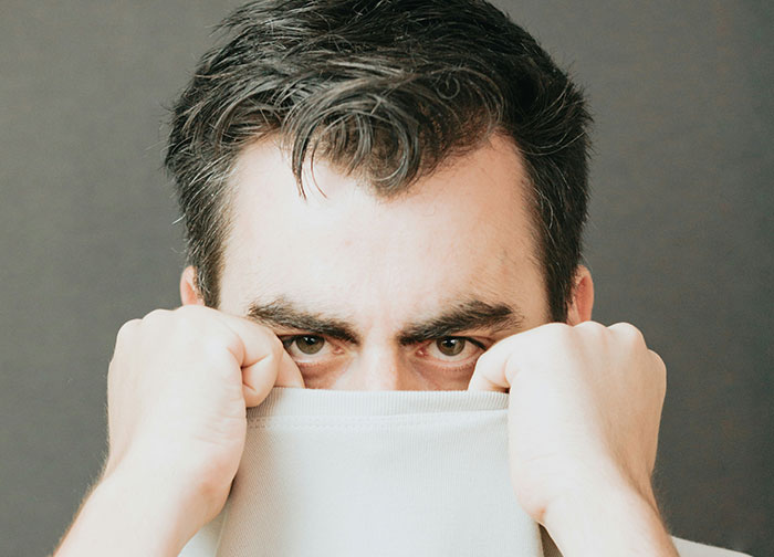 Man with intense eyes partially hiding face behind a shirt, symbolizing emotions faced by divorce lawyers in difficult cases.