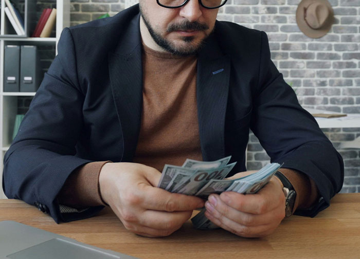 Divorce lawyer in office counting cash, wearing glasses and blazer, reflecting on challenging legal stories.