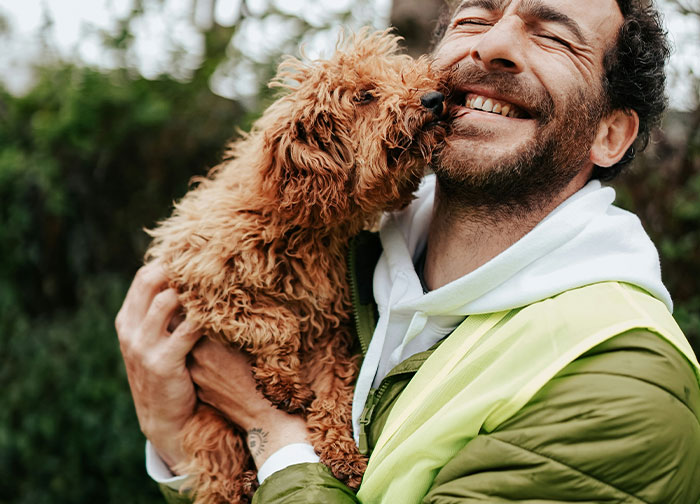 Man smiling and holding a small fluffy dog close, showing warmth and affection in an outdoor setting.