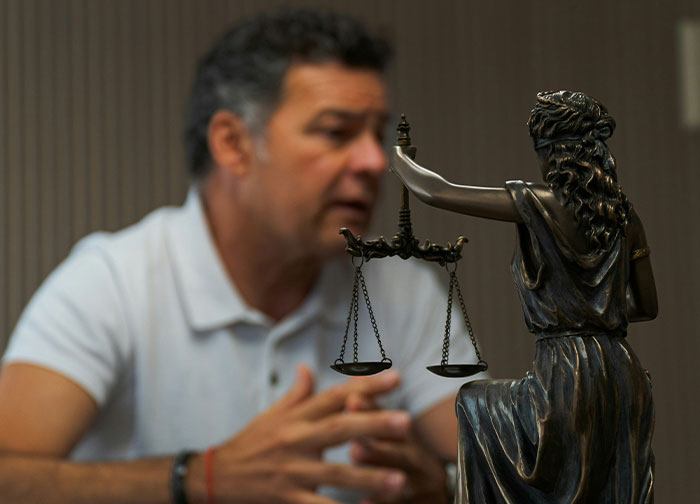 Man in white shirt discussing legal matters with Lady Justice statue, highlighting divorce lawyers and their haunting stories.