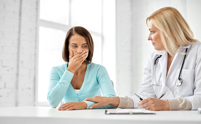 Woman in a teal sweater showing surprise while a female doctor in a white coat offers support during a medical consultation.
