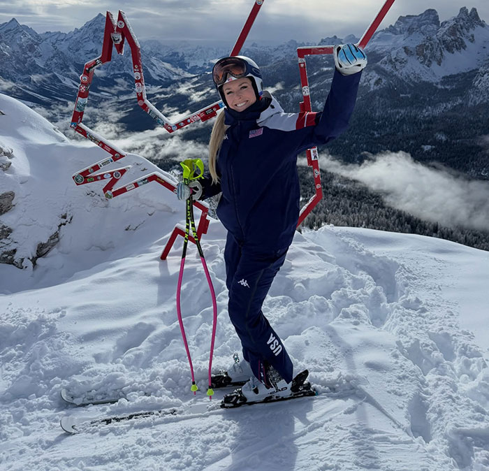 Lindsey Vonn skiing on snowy mountain celebrating after major update following horrific Olympics accident with ski poles raised.