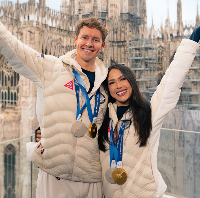 Two athletes wearing white jackets with Olympic medals, celebrating a French skater's suspicious win at the Olympics.