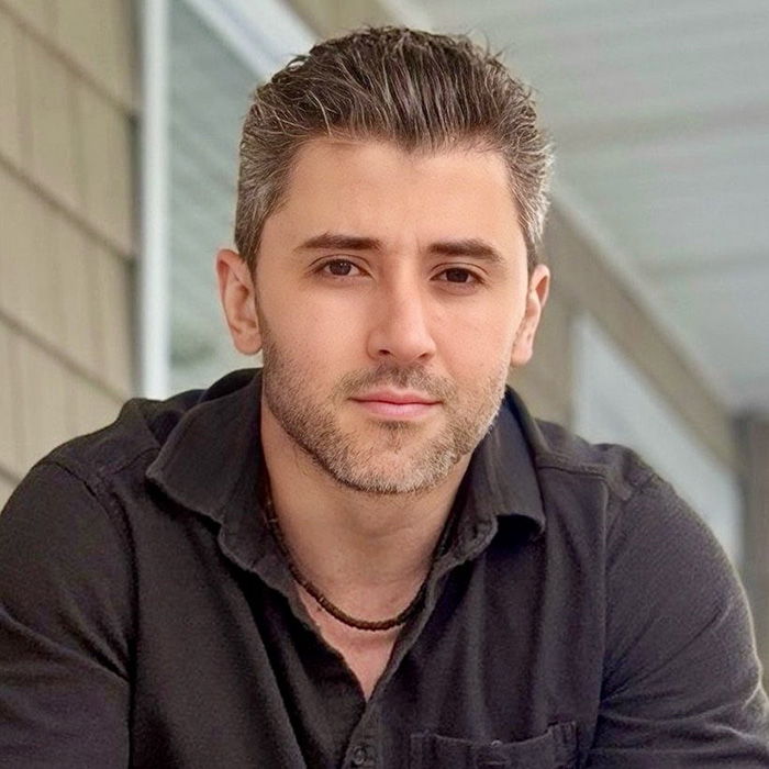 Young man with short hair and beard wearing black shirt, representing MAGA influencer involved in ICE detention story.