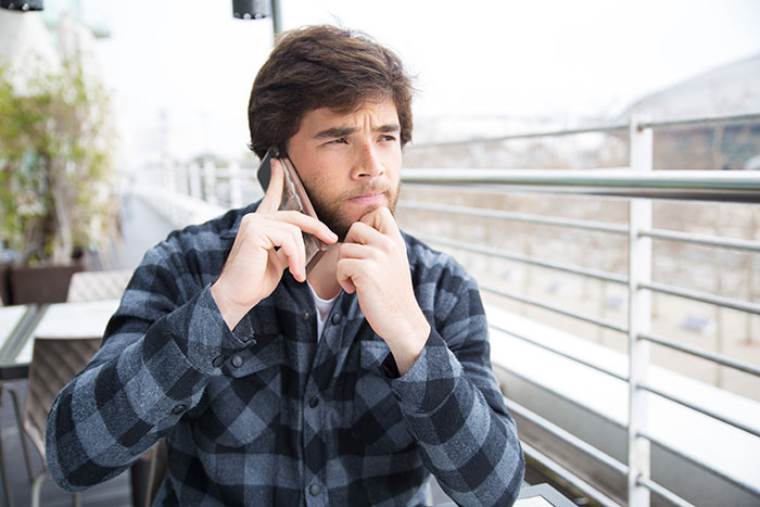 Man talking on phone with a thoughtful expression sitting outdoors, reflecting on single mom drama in dating life.