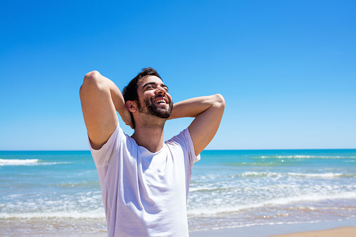 Man relaxing on the beach with hands behind head, smiling under blue sky, representing man date single mom drama.