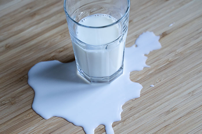Glass of spilled milk on wooden surface representing groom pranks causing unexpected wedding disruption.