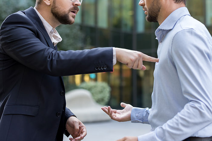Two men arguing outside in business casual attire, illustrating groom pranks and wedding conflict issues.
