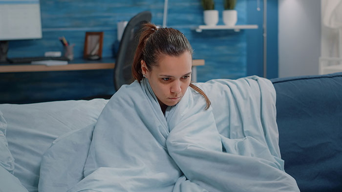 Woman wrapped in a blanket looking sad on a couch, depicting emotions tied to a man poly relationship with a depressed wife.