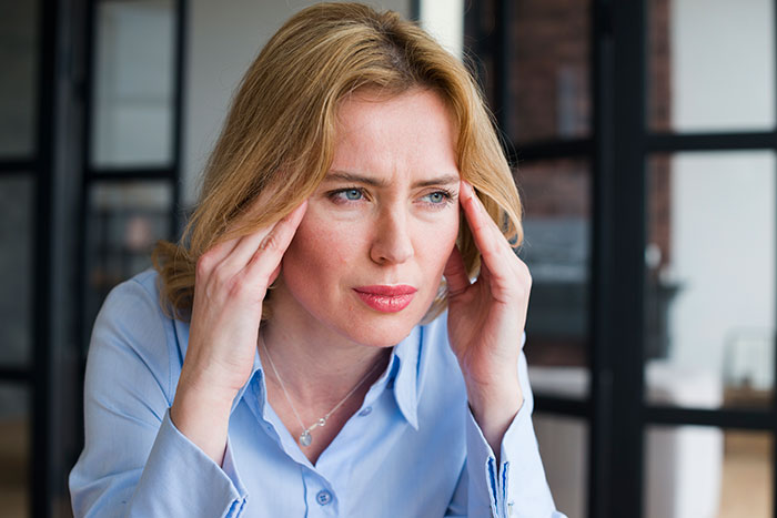 Woman with a stressed expression holding her temples, reflecting the challenges in a man poly relationship with a depressed wife
