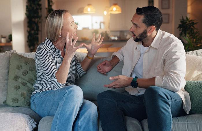Woman expressing frustration to man on couch in living room, depicting fat phobic mom and dad&rsquo;s mansplaining defense debate.