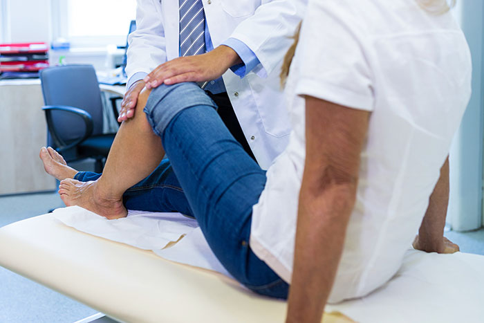 Doctor examining woman’s knee in a clinical setting highlighting concerns about medical misogyny and women’s health risks.