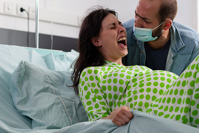 Woman in labor experiencing pain in hospital bed with partner beside her, highlighting medical misogyny impacting women’s health.