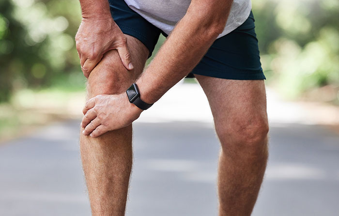 Man wearing smartwatch holding his knee in pain, illustrating medical misogyny impact on women’s health risks.