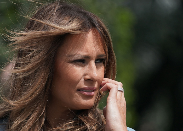 Melania Trump outdoors with wind blowing her hair, revealing a subtle hidden detail in her polished appearance.
