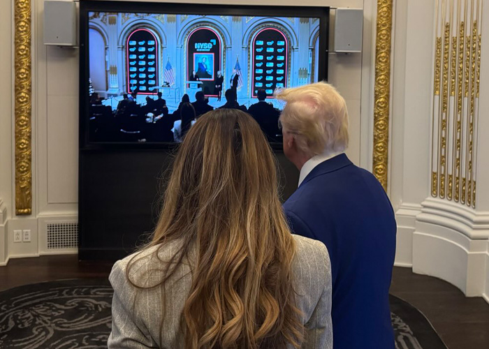 Melania Trump and Donald Trump watching a formal event on a large screen in an ornate room with gold details.