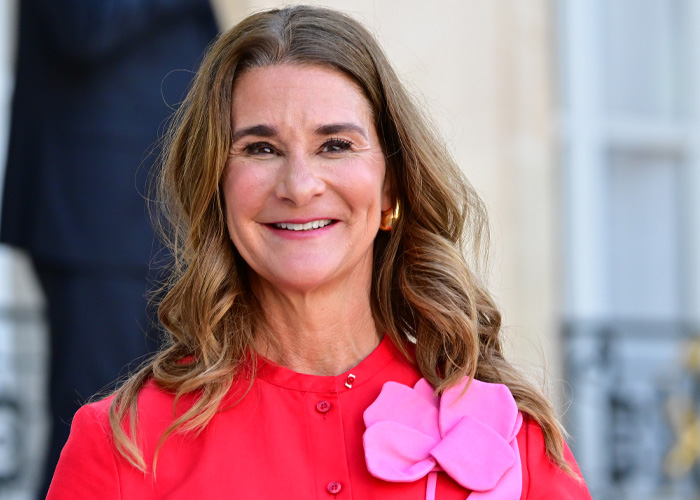 Melinda Gates smiling, wearing a red outfit with a pink flower, responding about forgiving Bill over Epstein files allegations.