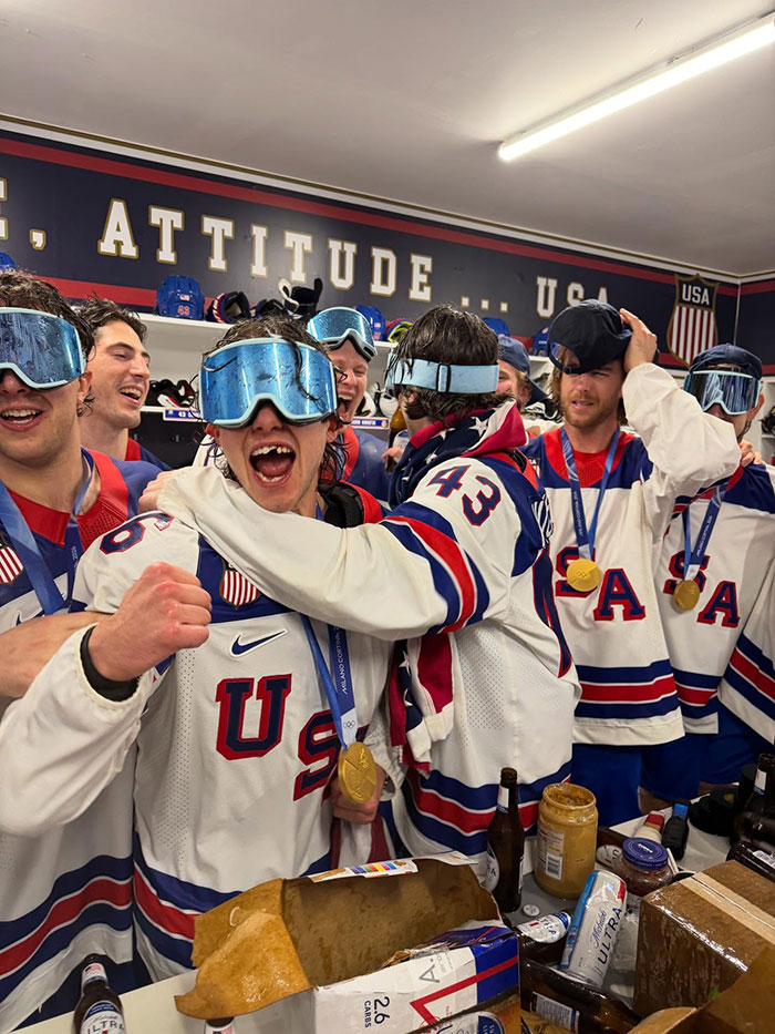US Olympics hero Jack Hughes celebrating with teammates wearing gold medals and protective goggles in a locker room setting. US Olympics hero Jack Hughes celebrating with teammates wearing gold medals and protective goggles in a locker room setting.