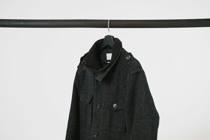 Dark gray coat hanging on a black hanger on a metal rod, illustrating underrated plane perks and travel attire benefits.