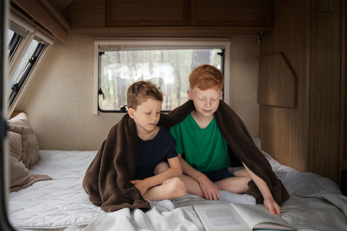 Two boys sitting under a blanket reading a book inside a camper, illustrating family tension and lack of sympathy themes.
