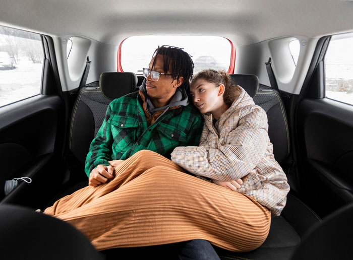 Couple sitting in car backseat, woman leaning on man, depicting troubled family dynamics and lack of sympathy after home loss.
