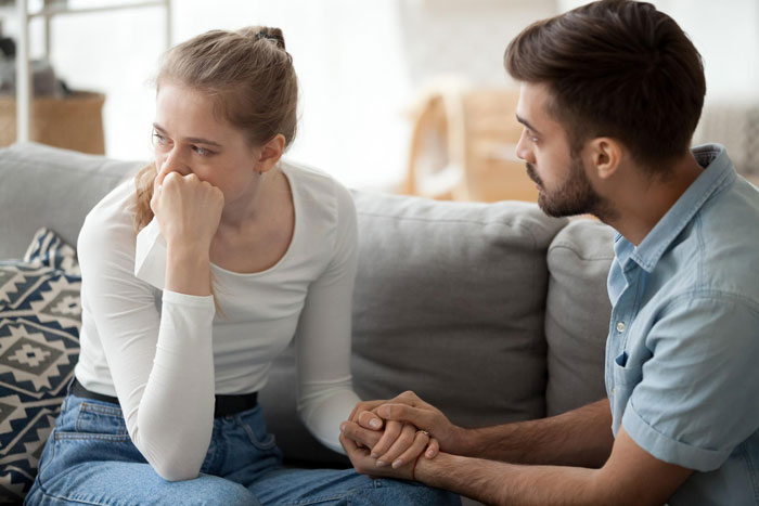 Young woman upset on couch while man comforts her, depicting emotional turmoil in family situation with evil MIL lies.