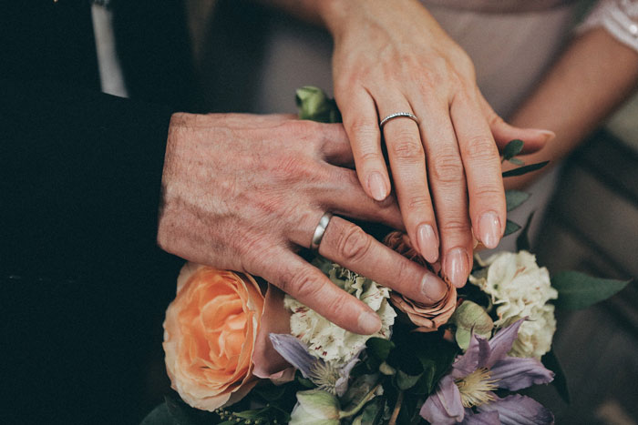Couple's hands with wedding rings resting on a colorful floral bouquet symbolizing their bond and emotional shock. Couple's hands with wedding rings resting on a colorful floral bouquet symbolizing their bond and emotional shock.