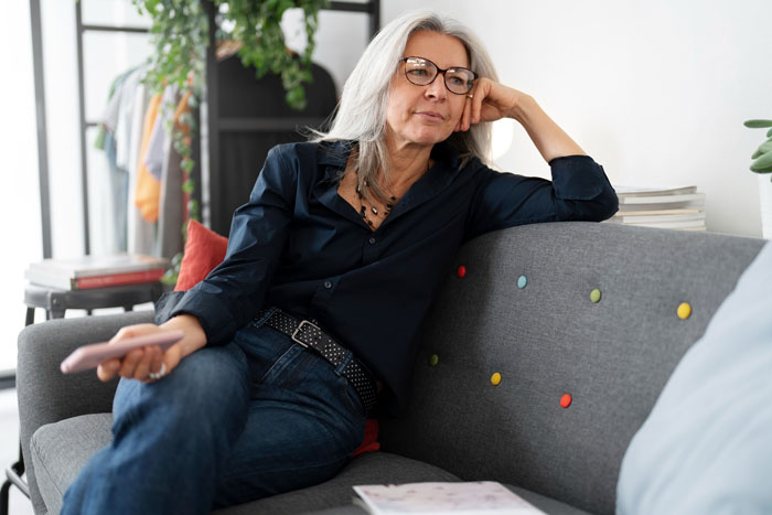 Middle-aged woman with glasses looking thoughtful on couch, reflecting MIL accusing DIL of changing son after wedding cut-off.