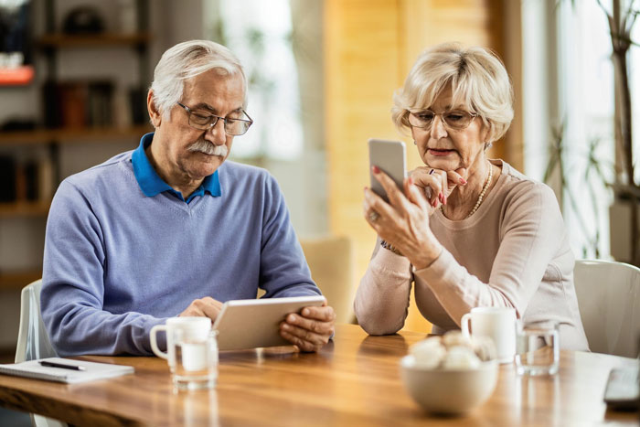 Elderly couple using digital devices, portraying tension related to MIL accusing DIL of changing him in a toxic family situation.
