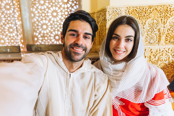 Young Muslim couple smiling and taking a selfie indoors with cultural decor, reflecting Muslim MIL concerns about culture. Young Muslim couple smiling and taking a selfie indoors with cultural decor, reflecting Muslim MIL concerns about culture.