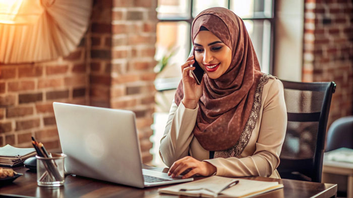 Young Muslim woman in hijab using laptop and phone in cozy office, reflecting on cultural and family traditions conflict. Young Muslim woman in hijab using laptop and phone in cozy office, reflecting on cultural and family traditions conflict.