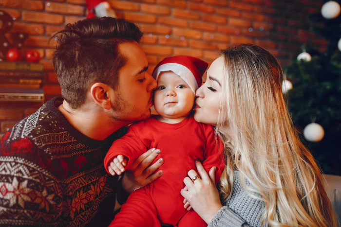 Young couple kissing their baby dressed in Christmas outfit, highlighting Muslim MIL conflict over cultural celebration. Young couple kissing their baby dressed in Christmas outfit, highlighting Muslim MIL conflict over cultural celebration.