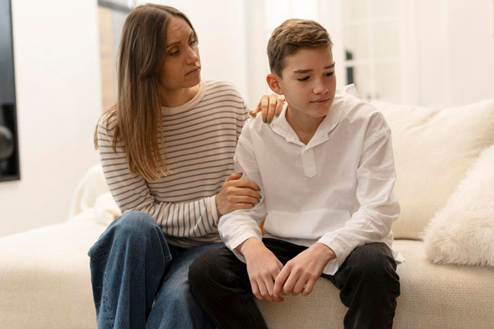 Mother comforting her son on the couch as he learns about family lies and his dad leaving before birth.