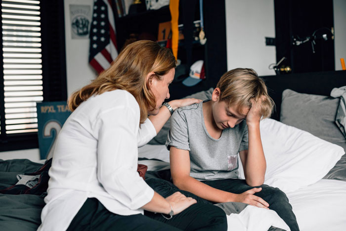 Mother comforting upset teenage son on bed, reflecting emotional moment related to dad leaving and family truth revealed.