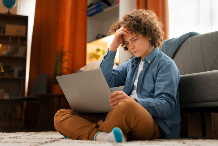 Young man sitting on floor with laptop looking confused and upset, discovering his mom may have been lying about his dad.