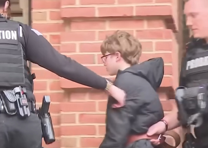 11-year-old accused escorted by officers outside brick building in case involving adoptive father’s slaying and heartbroken mom.