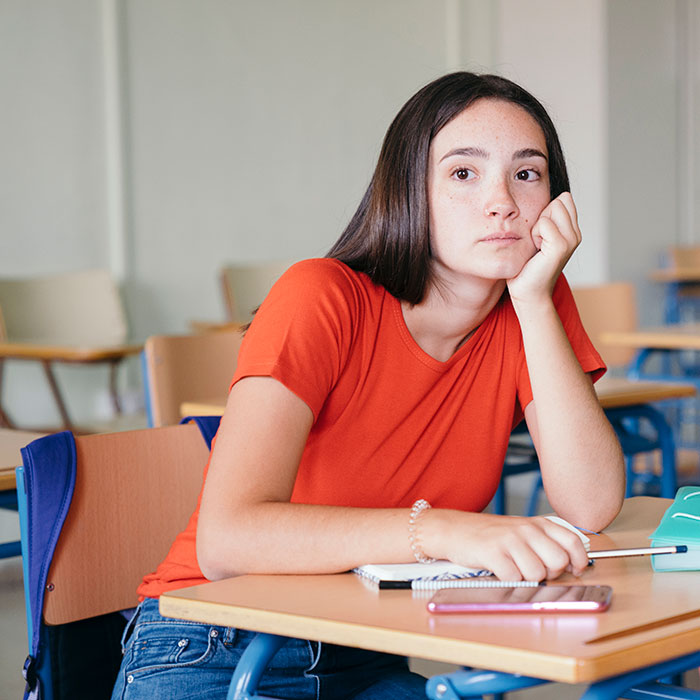 Student in an orange shirt looking thoughtful in a classroom, reflecting on disturbing things shared with teachers.
