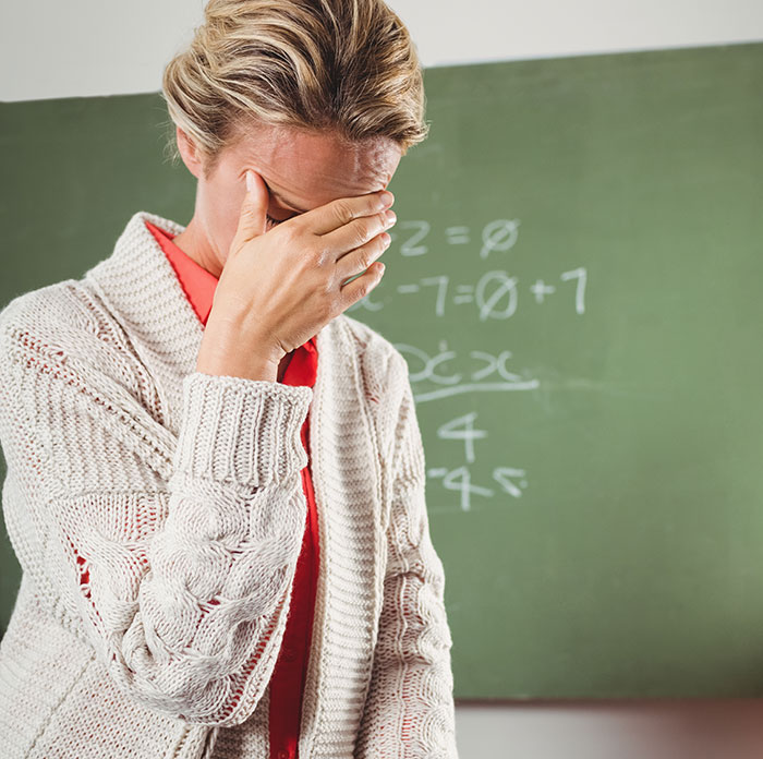 Teacher covering face, looking stressed in classroom, representing disturbing things students confided in teachers.