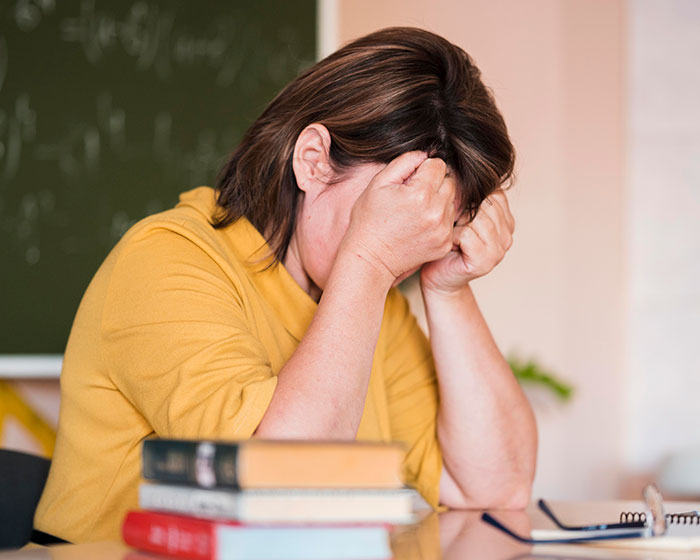 Teacher overwhelmed sitting with head in hands beside books, reflecting on disturbing student confessions shared in classroom.