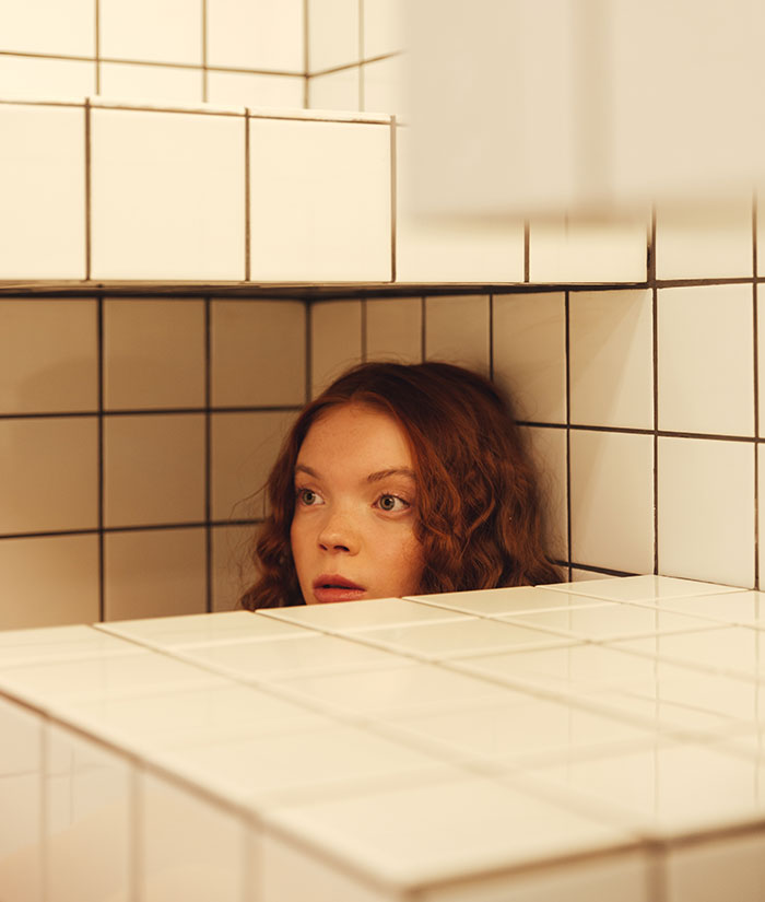 Young woman with red hair peeking from behind tiled walls, symbolizing students confiding disturbing secrets to teachers.