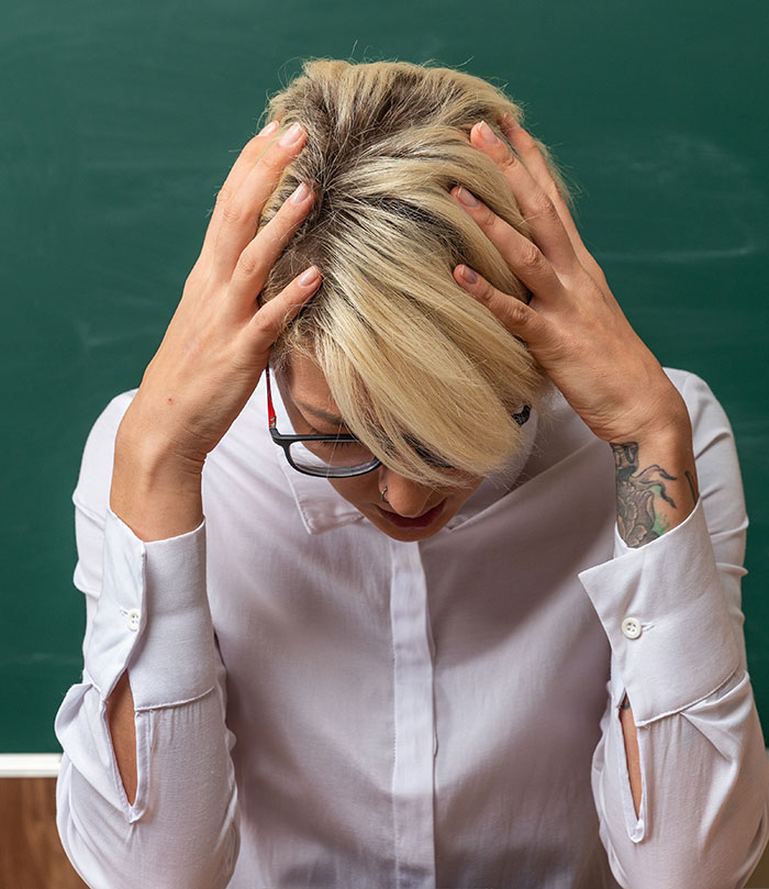 Stressed teacher holding head in classroom representing disturbing things students confided in teachers.