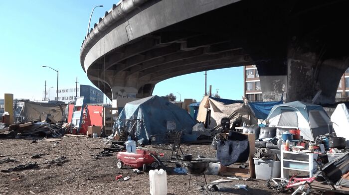 Homeless tents and debris under a highway overpass depicting a dystopian nightmare scene in an urban environment.
