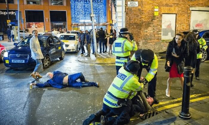Police restraining a person on the street while another lies on the ground in a dystopian nightmare city scene.